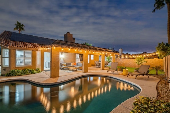 A pool with a patio area, a covered seating area, and a view of the surrounding landscape.