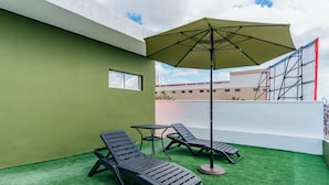 Una terraza en la azotea con césped artificial, dos sillones de relax, una mesa y un gran paraguas.