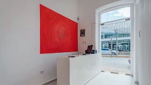 Un área de recepción con un escritorio blanco, un cuadro abstracto rojo de gran tamaño y vistas a la calle a través de puertas de vidrio.