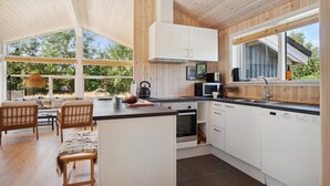 A modern kitchen with wooden cabinets, a dining area with a table and chairs, and large windows offering a view of the outdoors. - 3 bedroom awesome home in Gørlev (Gørlev)