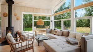 A cozy living room with a fireplace, wicker furniture, and large windows offering a view of the outdoors. - 3 bedroom awesome home in Gørlev (Gørlev)