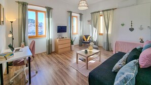Un salon chaleureux avec un plancher en bois, un canapé, une table basse, un bureau avec un ordinateur portable, une chaise et un téléviseur.