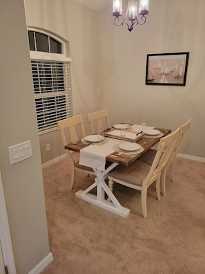 A dining room with a wooden table set for four, beige walls, a chandelier, and a framed picture on the wall.