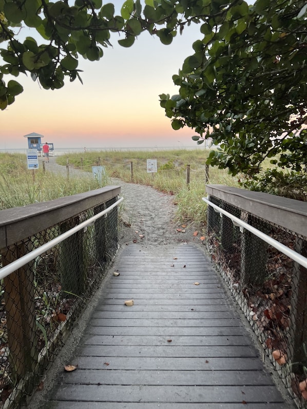 A wooden boardwalk leading to a beach area with a lifeguard tower in the distance.