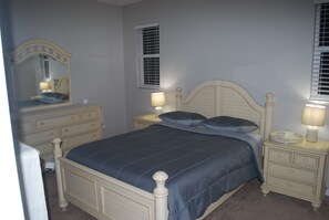 A bedroom with a bed, two bedside tables, a mirror, and a window with blinds.