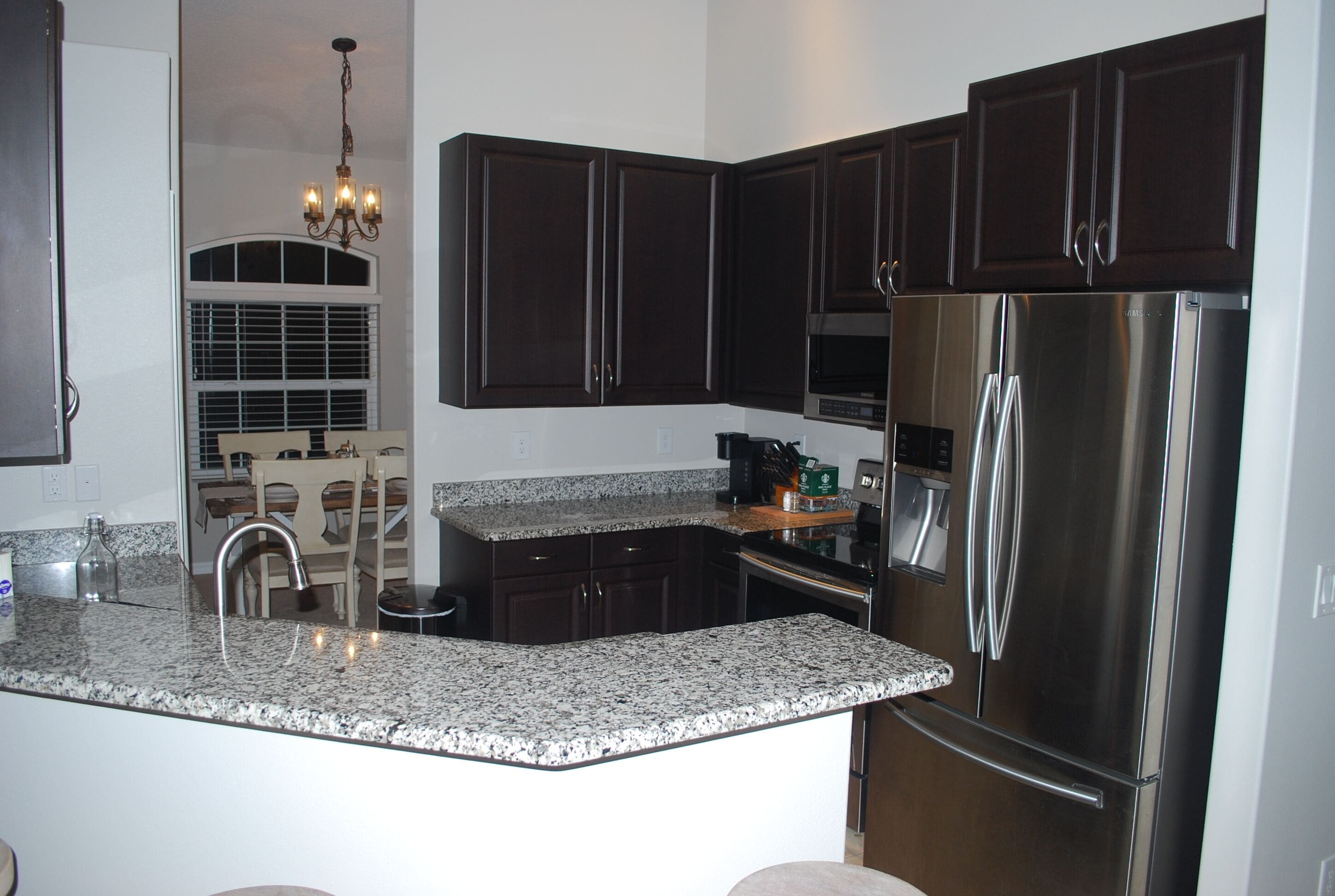 A kitchen with dark wood cabinets, a stainless steel refrigerator, granite countertops, and a built-in oven.
