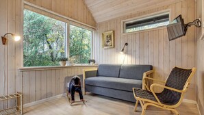 Una habitación acogedora con un sofá gris, una silla de madera, una mesita con una planta y un cuadro en la pared.