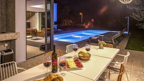 An outdoor dining area with a pool, table set with bread, wine, and flowers. - Stunning home in Donji Prolozac with sauna (Donji Prolozac)