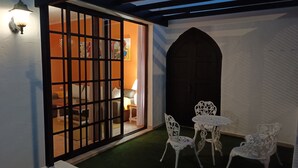 Una habitación con un gran ventanal corredero que da a una cama, una pequeña mesa con sillas y un arco decorativo.