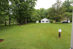 A grassy yard with a small white building, trees, and a person holding a sign. - Pymatuning Lake Walking distance to Espyville Marina! (Pymatuning Central)