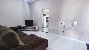 Un salon moderne avec un canapé marron, un téléviseur à écran plat et un sol carrelé de couleur blanche.