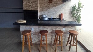 Une cuisine avec un plan de travail noir, quatre tabourets en bois et un mur de fond en briques.