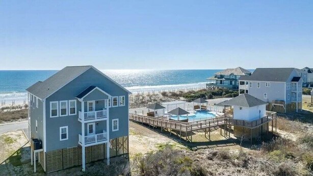 Une propriété située en bord de mer, comprenant une maison à deux étages, une piscine et une terrasse en bois.