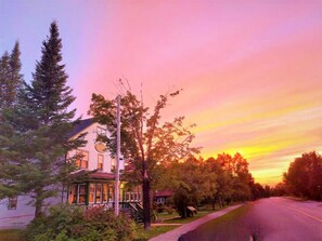 A two-story house with a porch, surrounded by trees and a road. - Auberge l'Orpailleur (Val-d'Or)