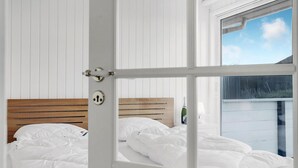 Makuuhuoneessa on puinen sängynpääty, valkoiset vuodevaatteet ja ikkunasta avautuu näkymä valkoiseen rakennukseen.