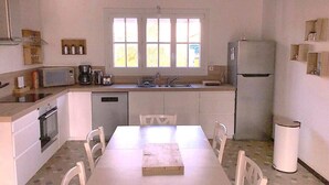 A compact kitchen with white cabinets, a dining table, and a window above the sink. - Le Clos de la Guittière - 6 people (Talmont-Saint-Hilaire)