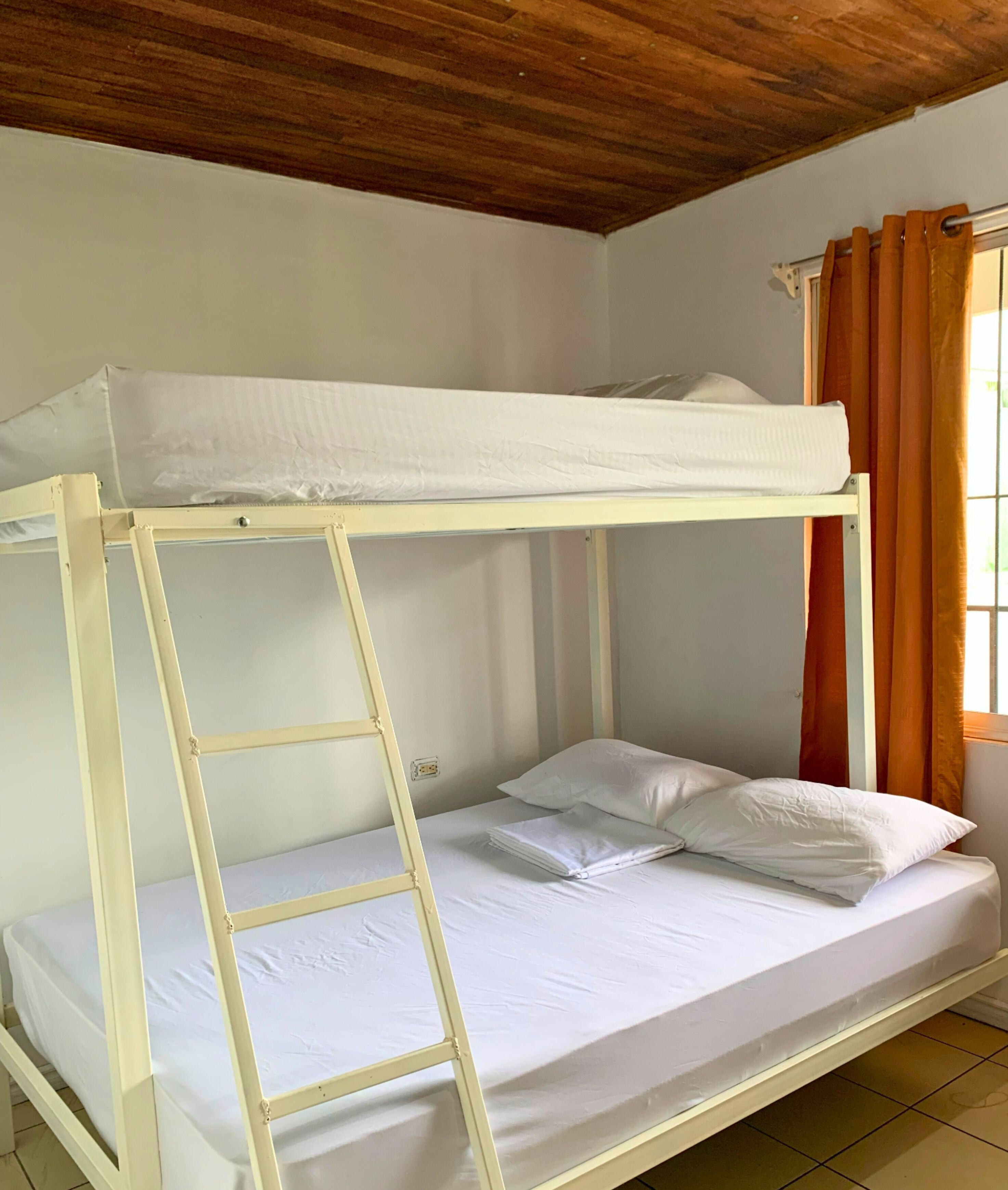 A bunk bed with a ladder, white bedding, and orange curtains.