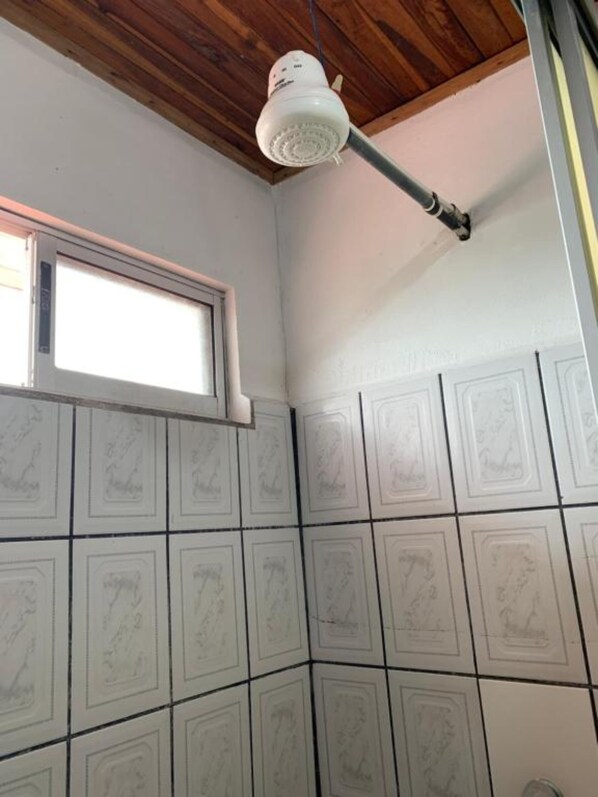 A bathroom with white tiles featuring embossed designs, a window, and a ceiling-mounted shower fixture. - Arenal Sloth Hostel (La Fortuna)