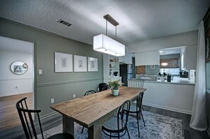 Una cocina moderna con armarios blancos, una mesa de comedor de madera y una lámpara colgante.