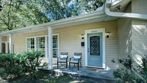A house with a beige exterior, a blue door with the number 4035, two chairs on the porch, and a small garden area. - Serene Home in Fondren Location Near Hospitals (Jackson)