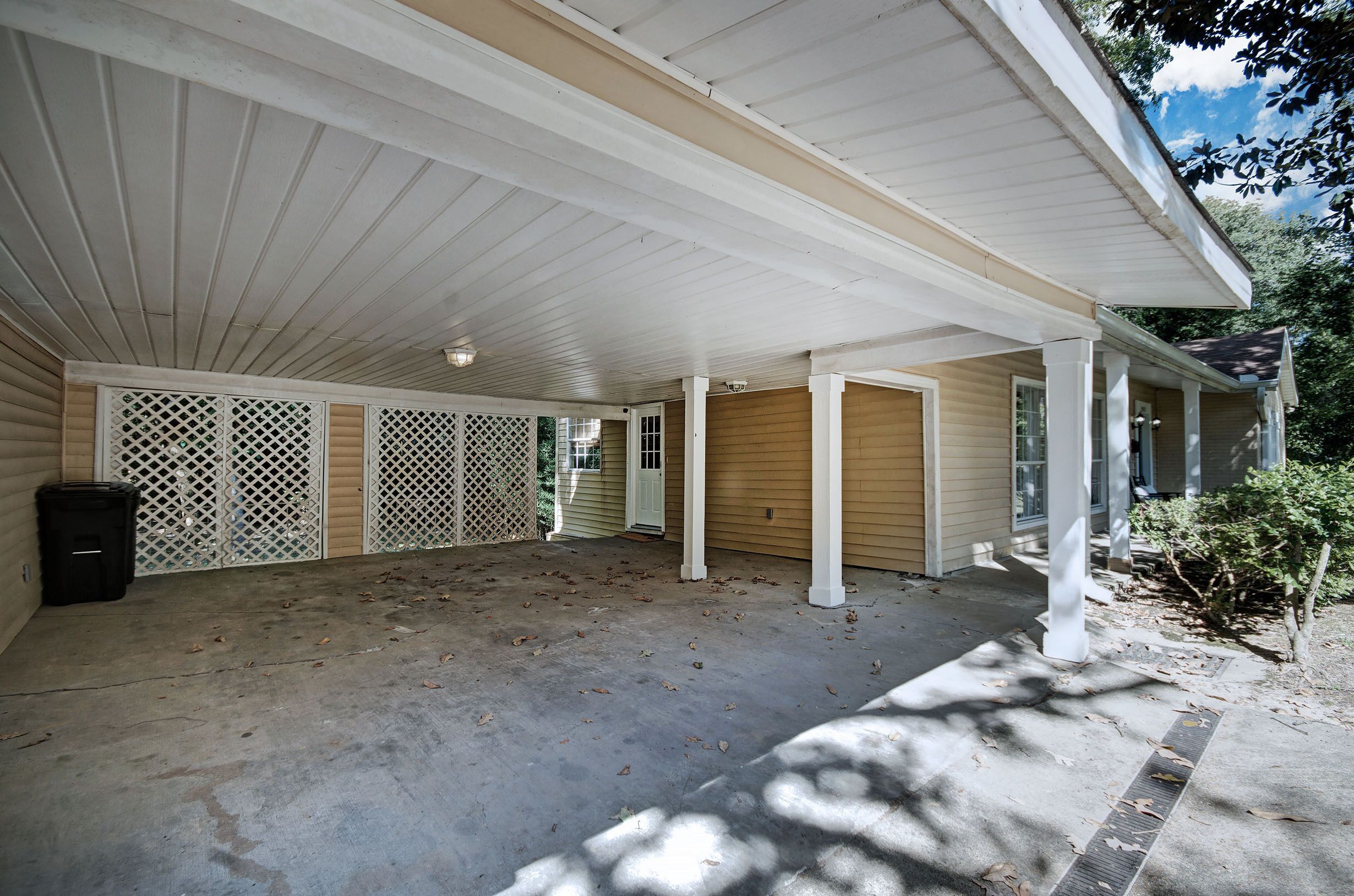 A covered porch with a concrete floor, white columns, and a wooden door.