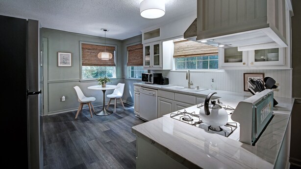 A modern kitchen with white cabinets, a gas stove, a microwave, and a dishwasher. There is a dining area with a table and chairs. - Serene Home in Fondren Location Near Hospitals (Jackson)