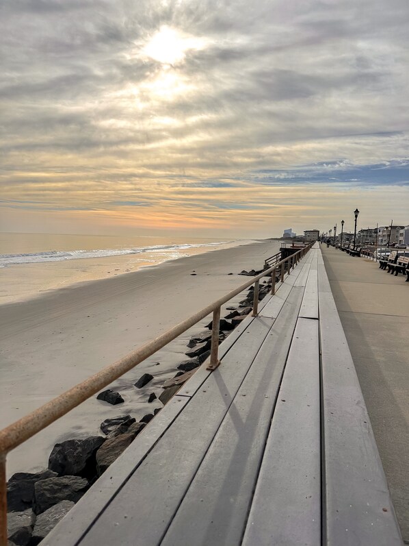 A boardwalk with a railing, leading to a beach with waves and a cloudy sky.