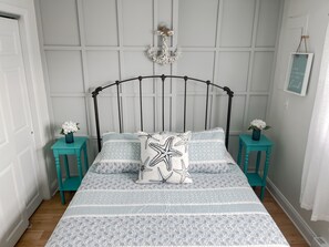 A neatly arranged bedroom with a bed centered against a paneled wall, flanked by two small teal nightstands with lamps.