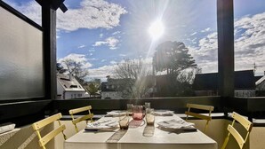 A dining table with chairs, a glass pitcher, and a glass on a balcony with a view of houses and trees. - Carnac 3 Pièces Duplex, 4 Personnes 150m Plage (CARNAC)