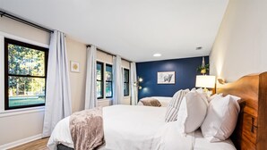 Une chambre à coucher avec un lit, une fenêtre avec des rideaux, une lampe fixée au mur et un tableau encadré.