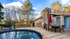 Une terrasse en bois avec une piscine, des espaces de détente en plein air et un bâtiment en briques doté de grandes fenêtres.
