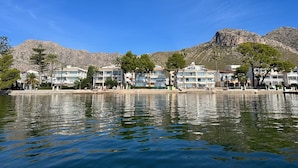 A coastal hotel with multiple balconies, a mountain backdrop, and a calm sea in the foreground. - Holiday home Balaixa 8 by the sea (Puerto Pollensa)
