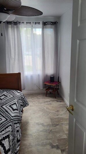 A bedroom with a bed, a small table with a speaker, and a door.
