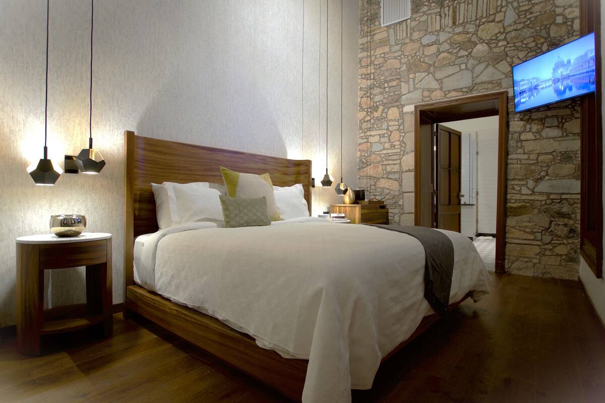 Ein Schlafzimmer mit einem hölzernen Bett, weißer Bettwäsche, einer Steinsäule und einem an der Wand montierten Fernseher.