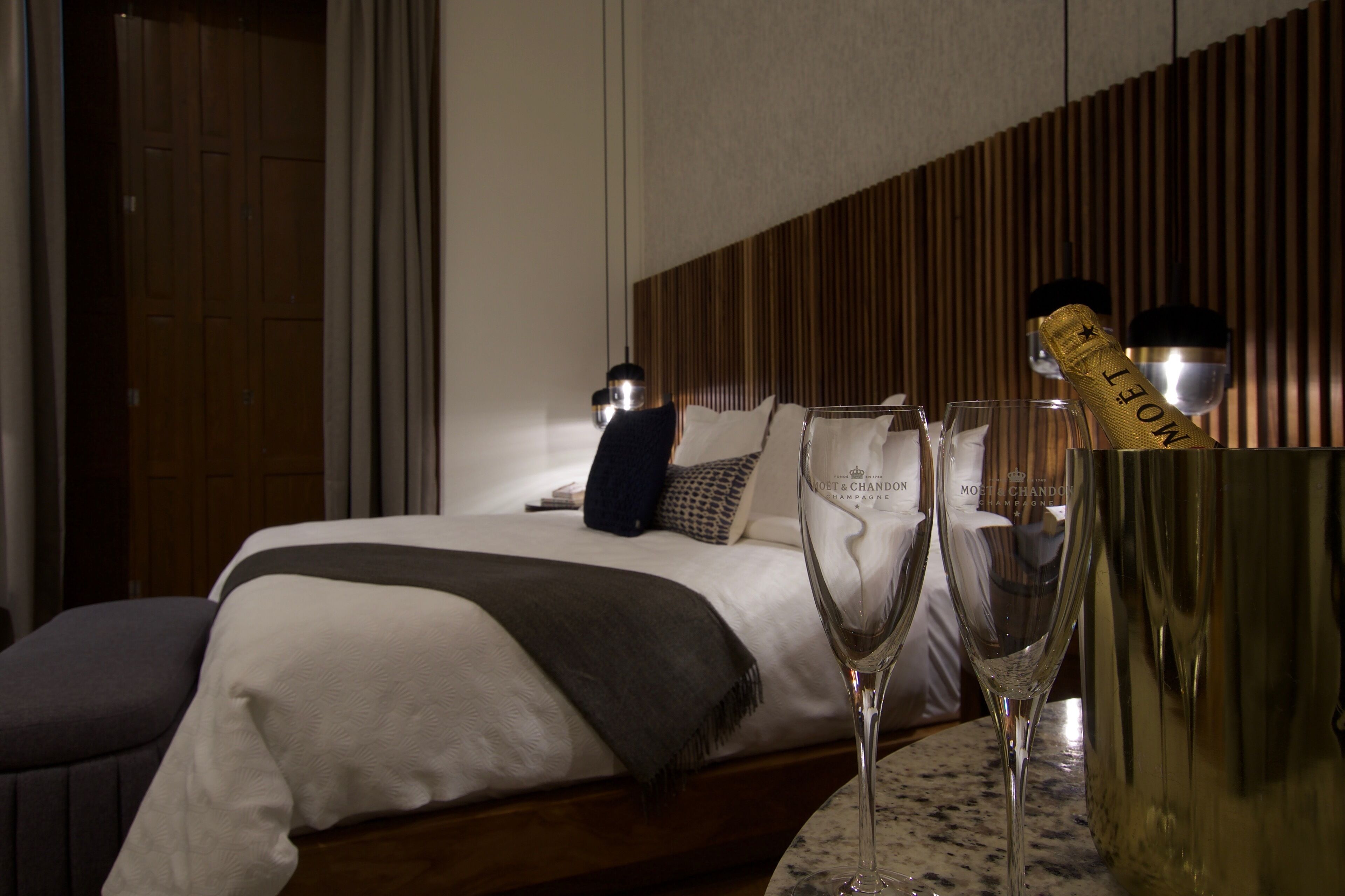 Una habitación de hotel con una cama bien hecha, un minibar y una botella de champán.