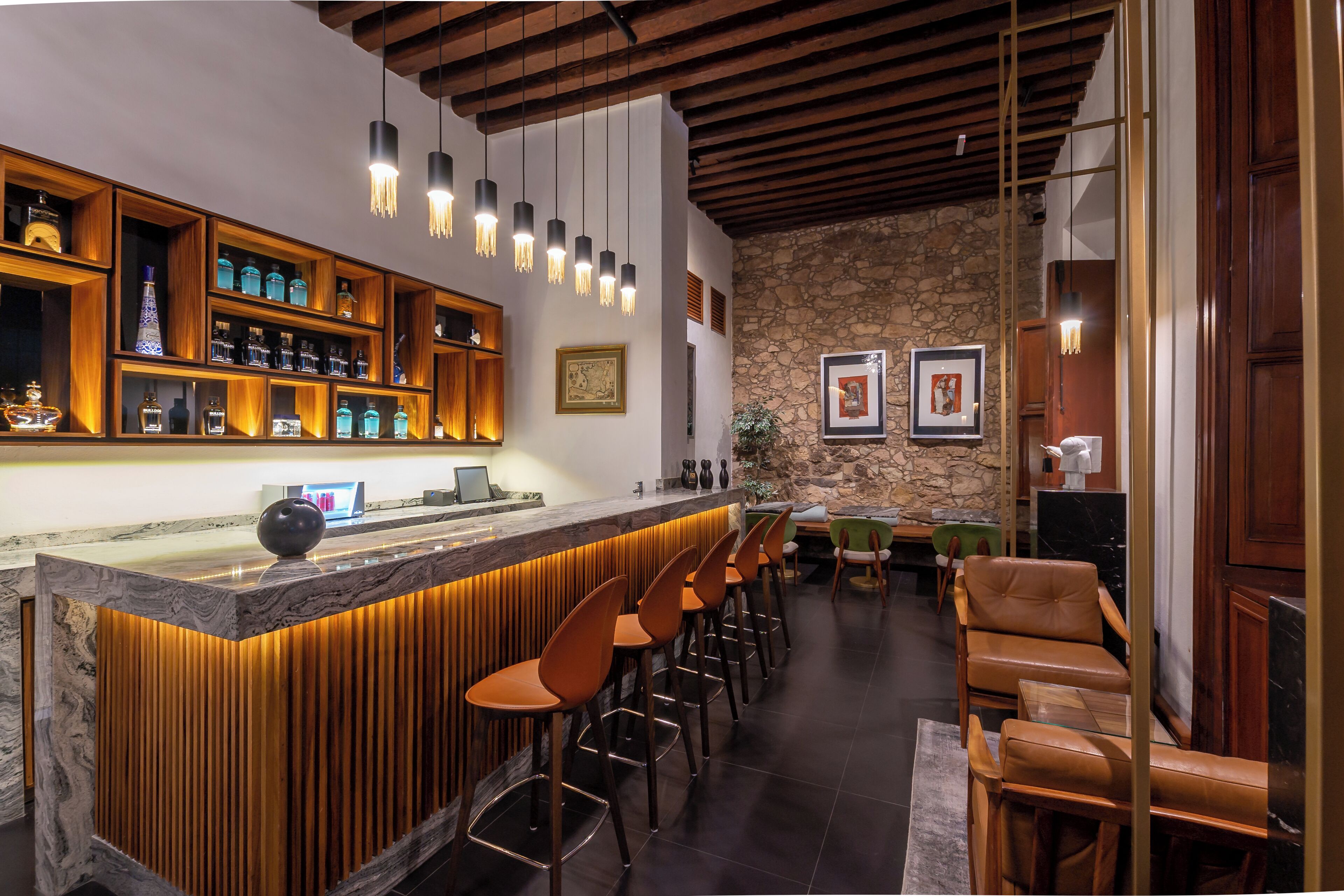 Un espace bar avec des étagères en bois, des luminaires suspendus et des fauteuils en cuir.