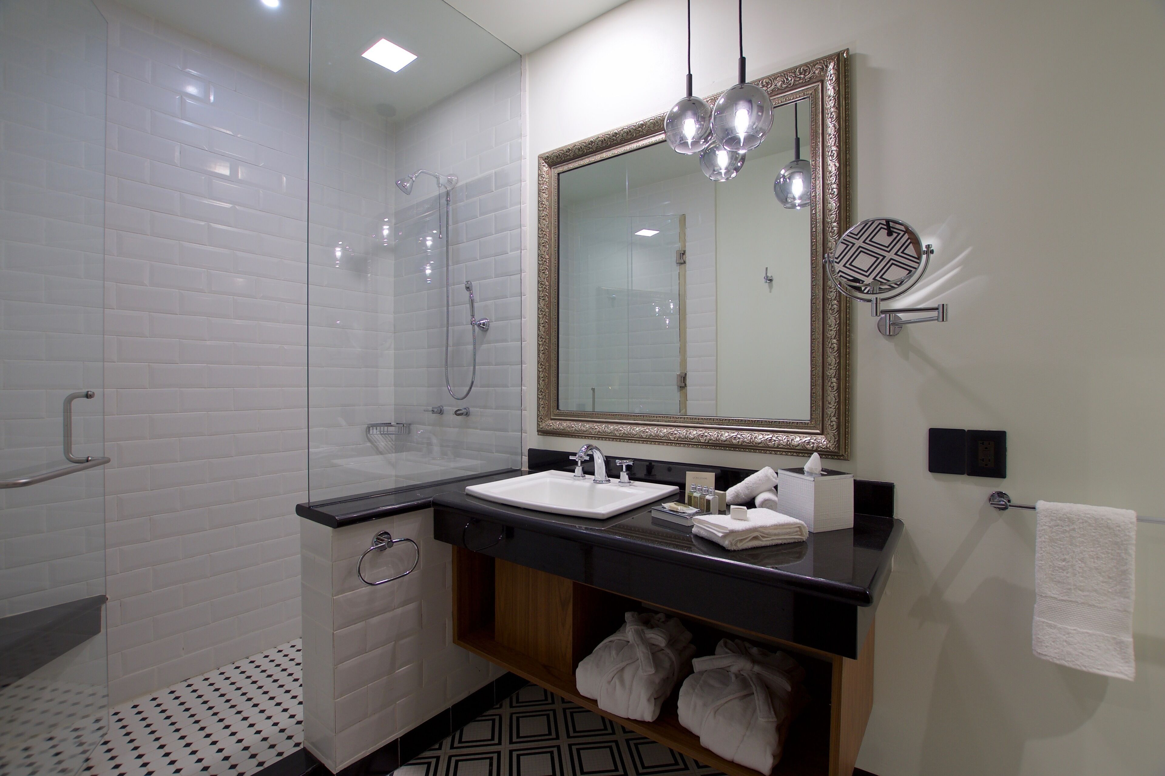 A modern bathroom with a glass-enclosed shower, a white sink with a black countertop, and a large mirror with a decorative frame.