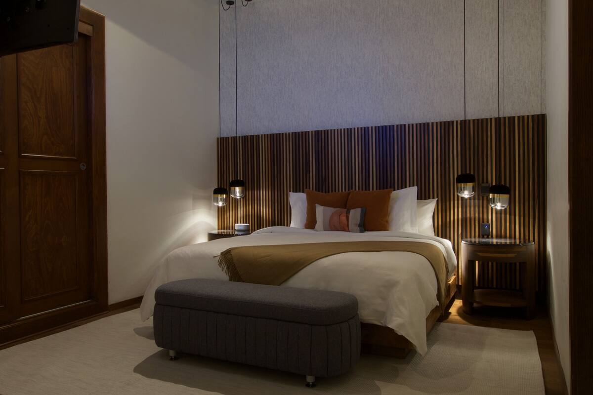 Ein Schlafzimmer mit Bett, Nachttischlampen, einer Bank und einem Holzschrank.