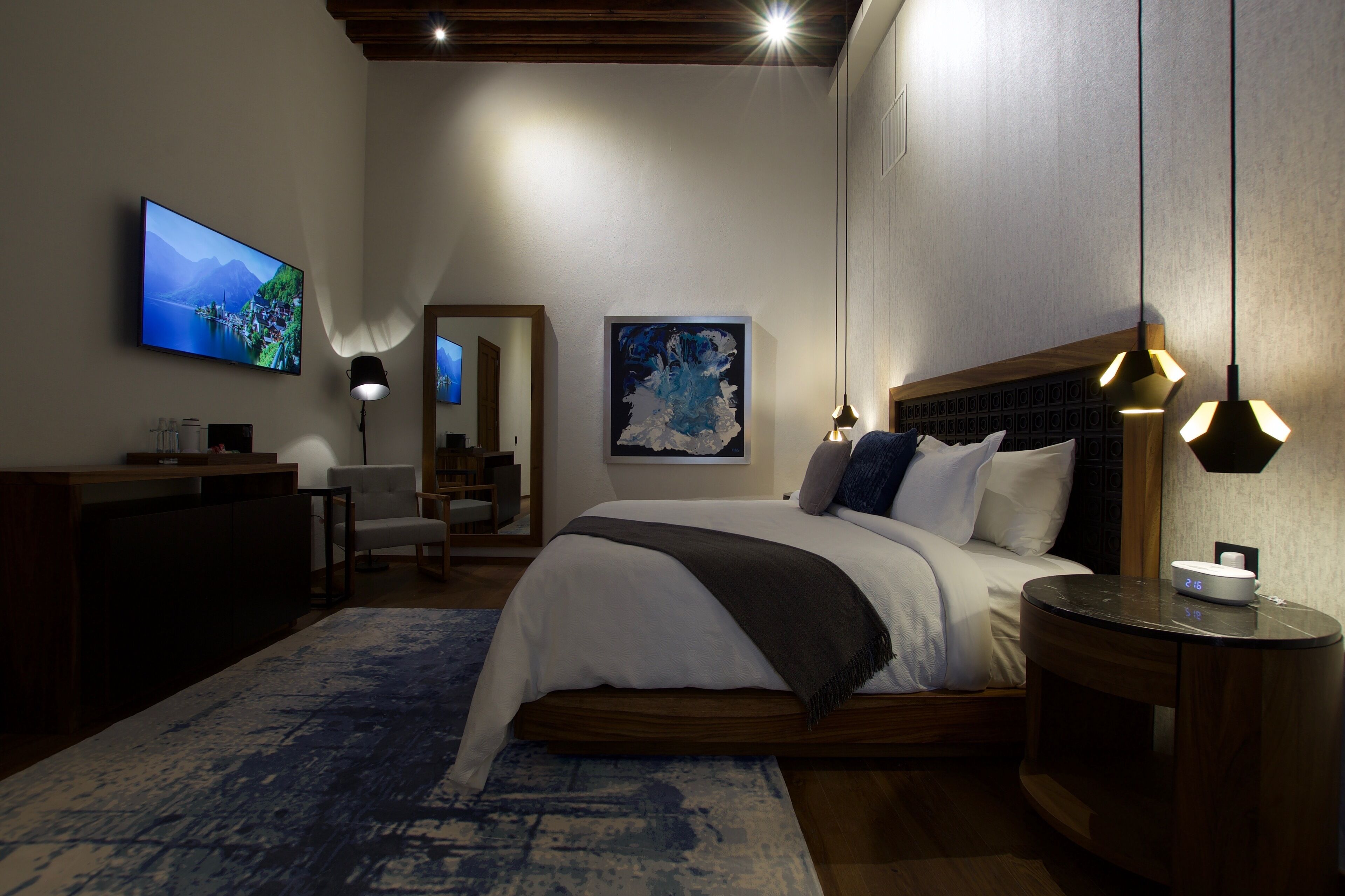 Un dormitorio moderno con una cama grande, un escritorio, una silla, un televisor y obras de arte en las paredes.