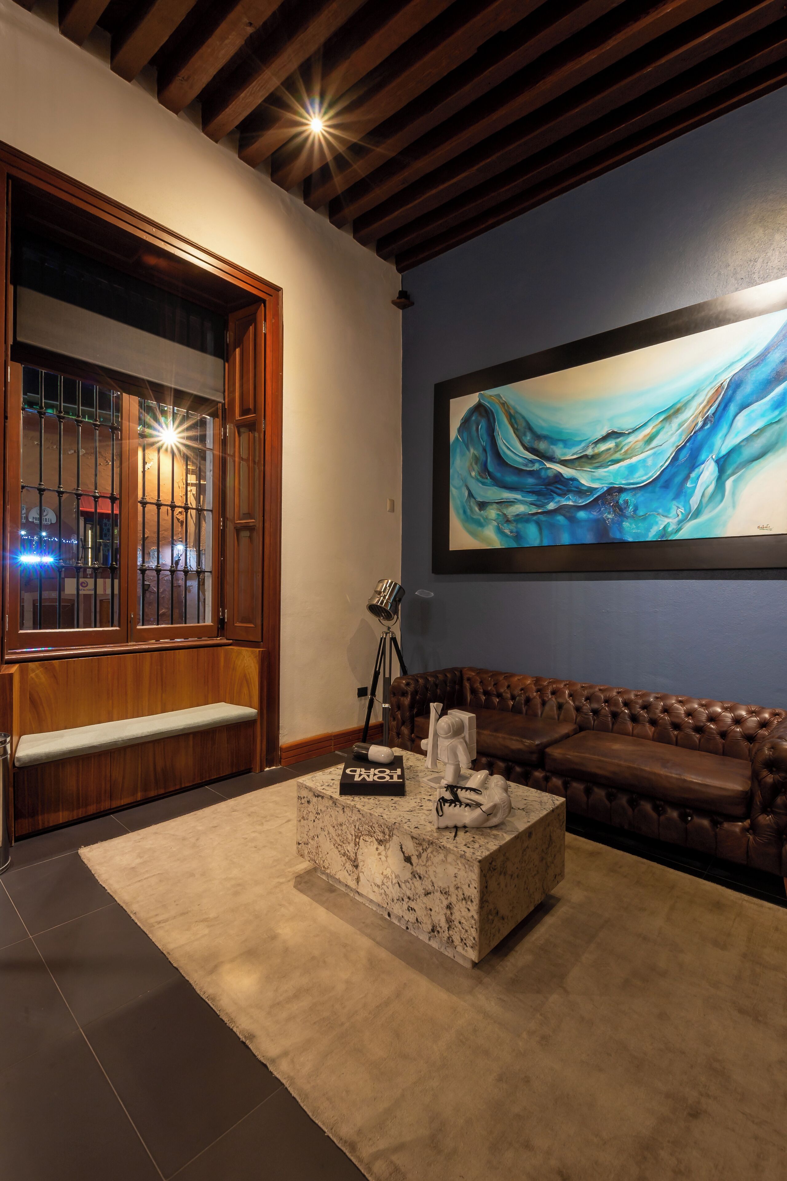 A cozy living room with a wooden bench, a marble coffee table, and a large abstract painting on the wall.