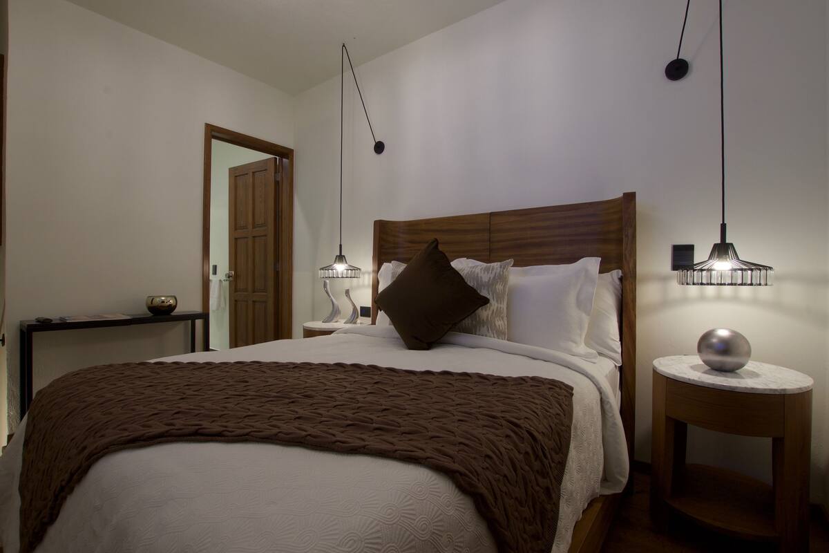 Ein ordentlich bezogenes Bett mit einer braunen Decke, einem hölzernen Kopfteil und zwei Nachttischlampen.