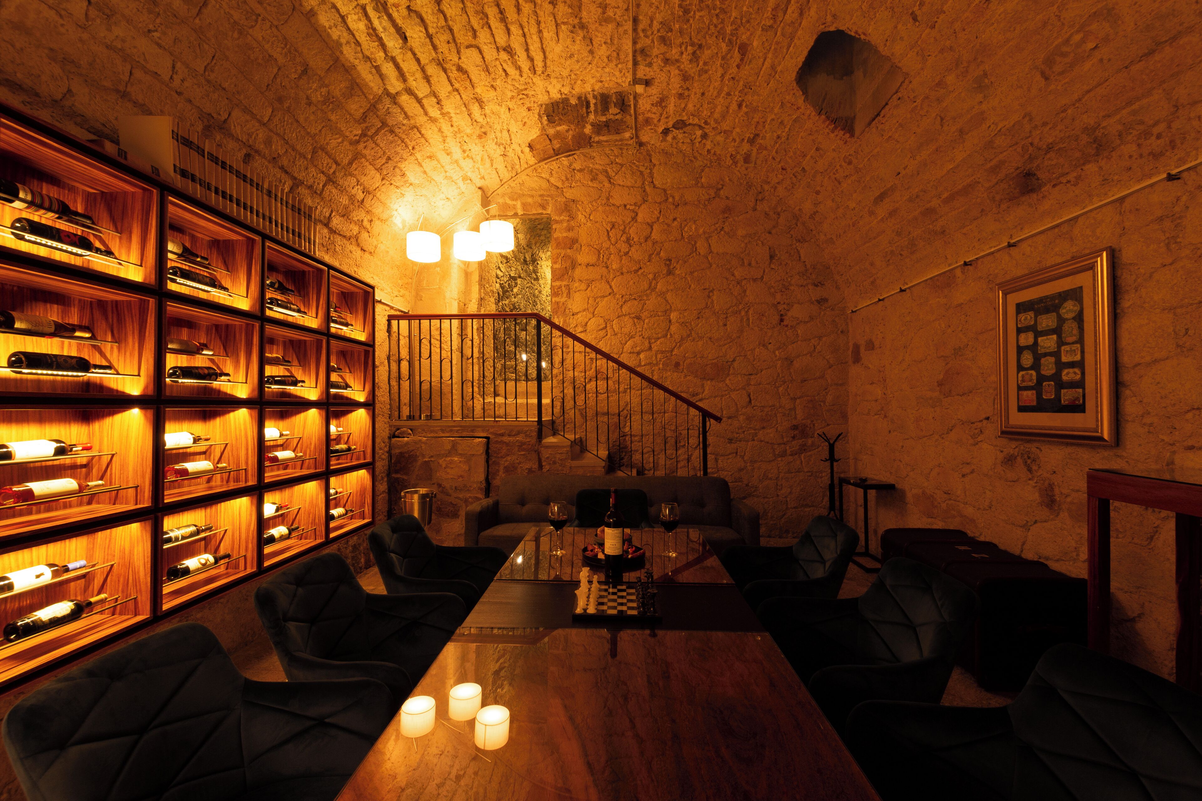 A cozy room with a wooden table, leather chairs, a bookshelf with wine bottles, and a staircase.