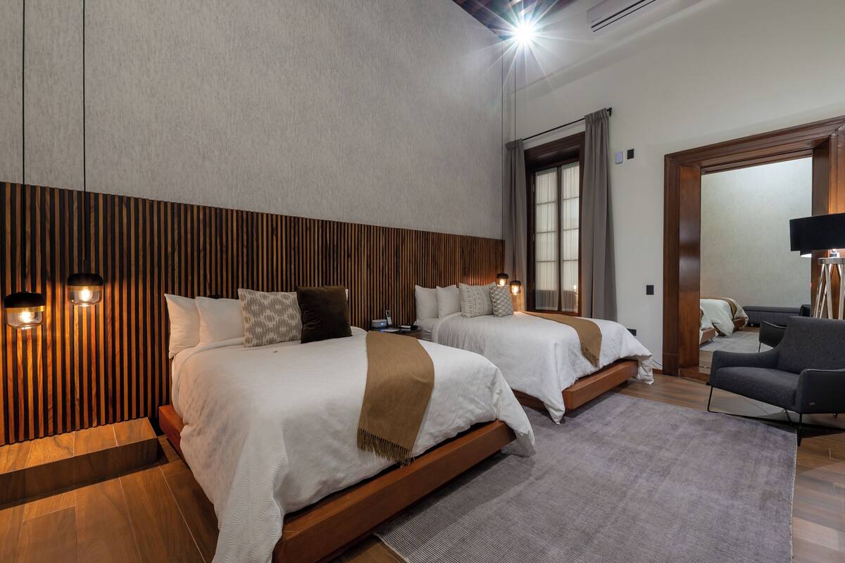 Ein modernes Hotelzimmer mit zwei Betten, einem Schlafsofa, einem Flachbildfernseher und einer Wand mit Holzverkleidung.