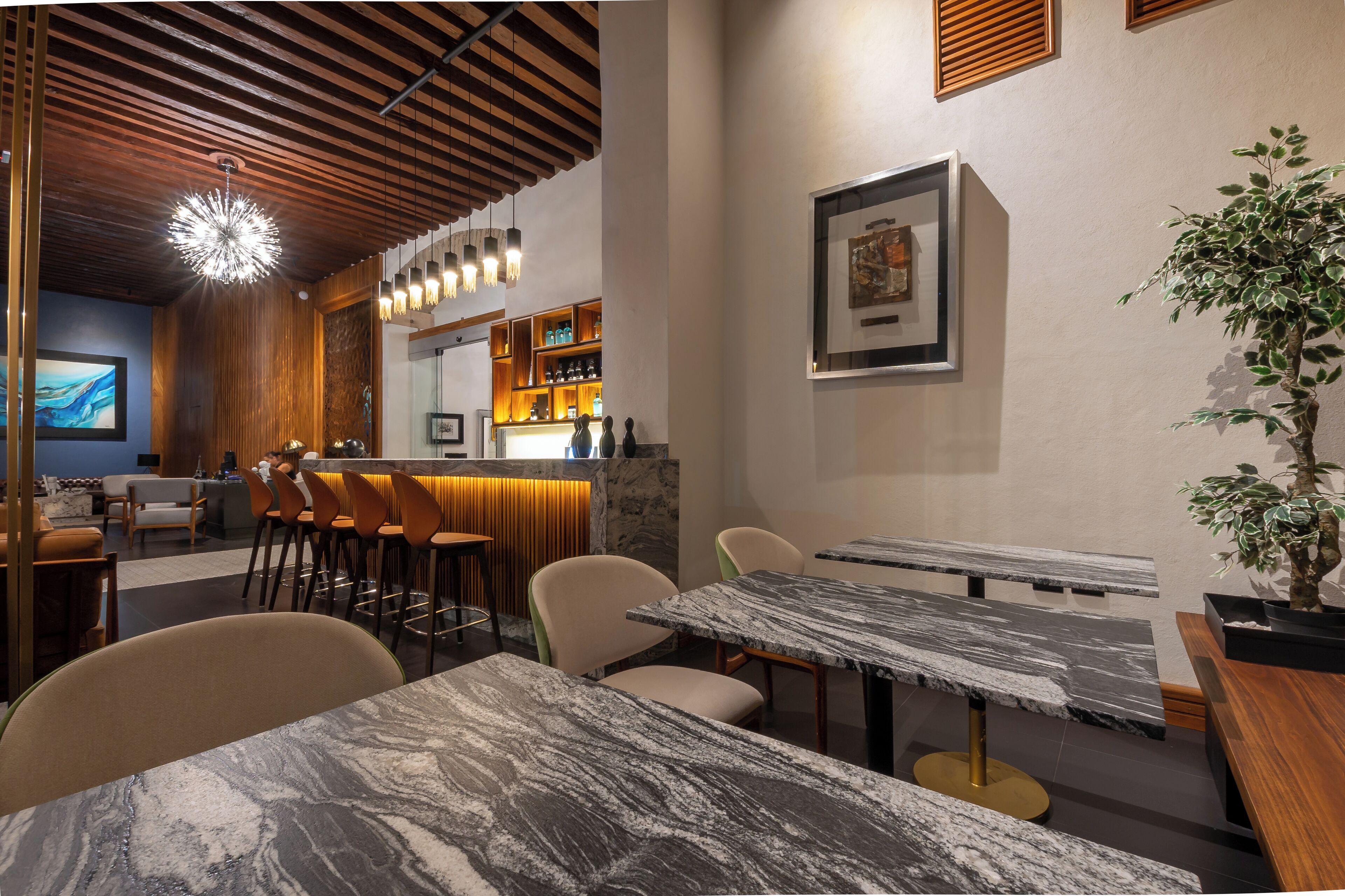 A modern restaurant with marble tables, wooden ceiling, and a bar area with stools.