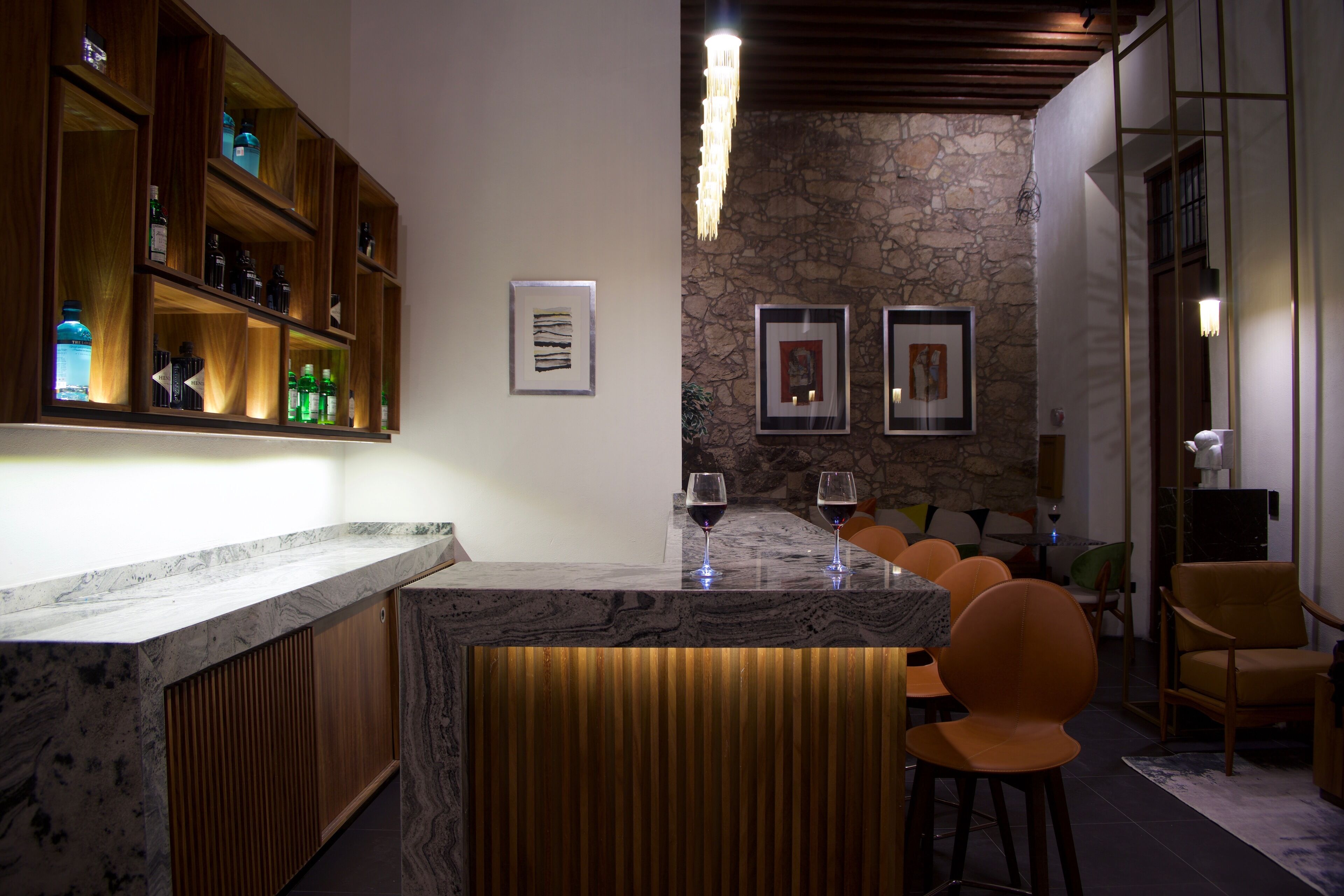 A bar area with a marble countertop, wooden shelves with bottles, and two framed artworks on the wall.