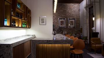 A bar area with a marble countertop, wooden shelves with bottles, and two framed artworks on the wall.