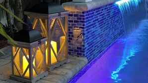 A pool with a blue-lit waterfall, a tiled wall, and two lit lanterns. - House has power ,Fast WIFI，Near Anna Maria beach (Bradenton)