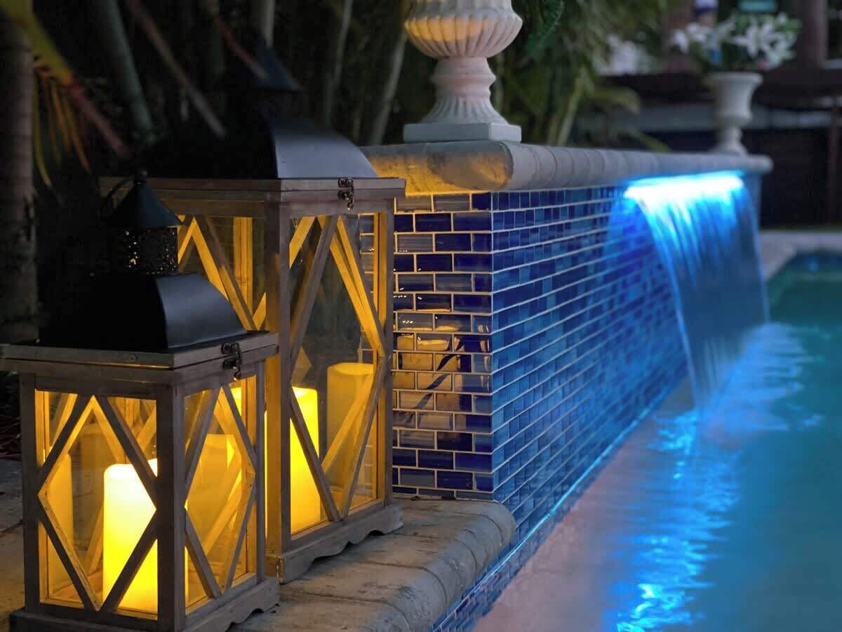 A pool with a blue-tiled edge, a white balustrade, and two lit lanterns.