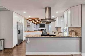 A modern kitchen with white cabinets, a stainless steel range hood, and a central island.