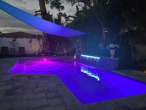 A swimming pool with a water feature and a blue canopy.
